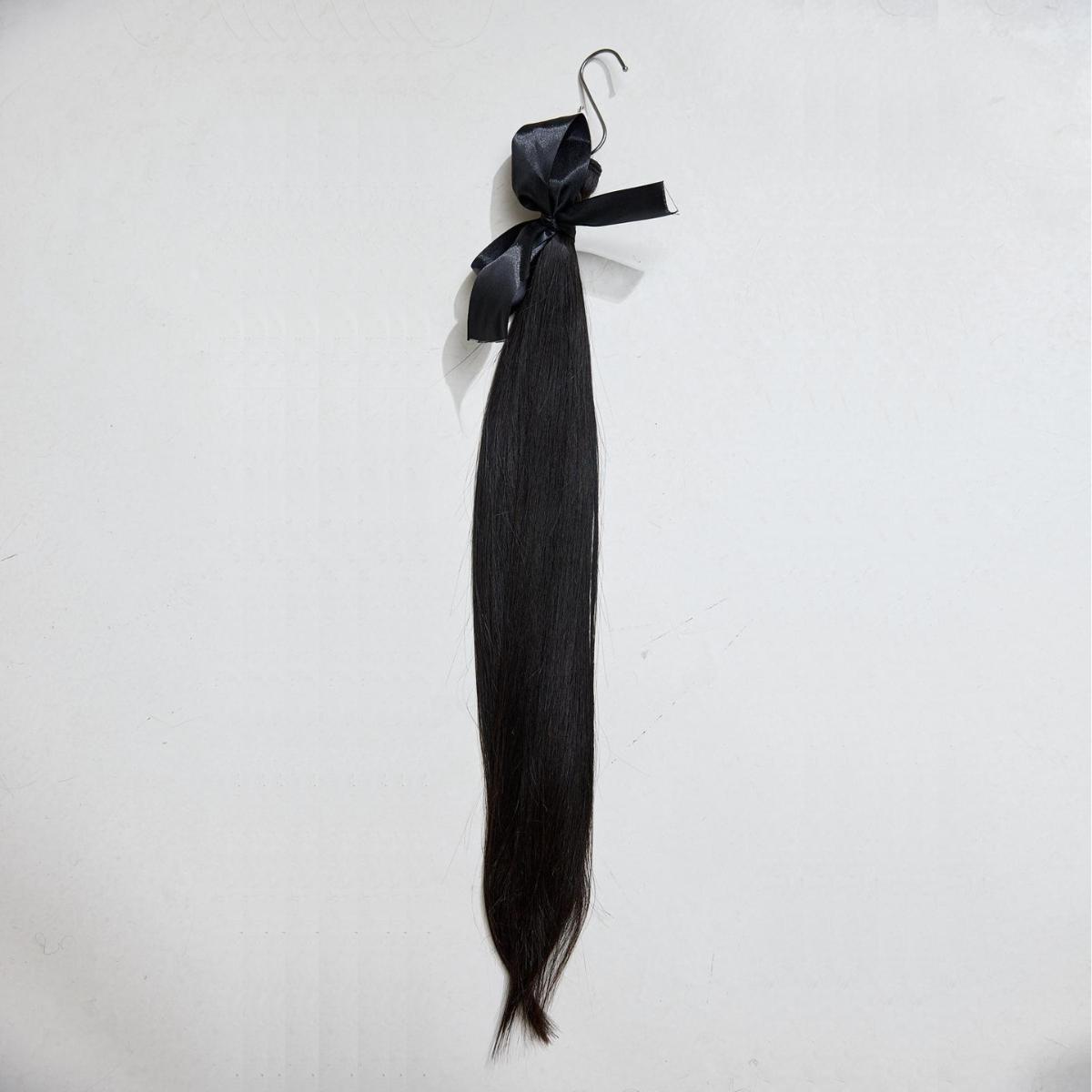 Black hair extensions on a hanger against a white background