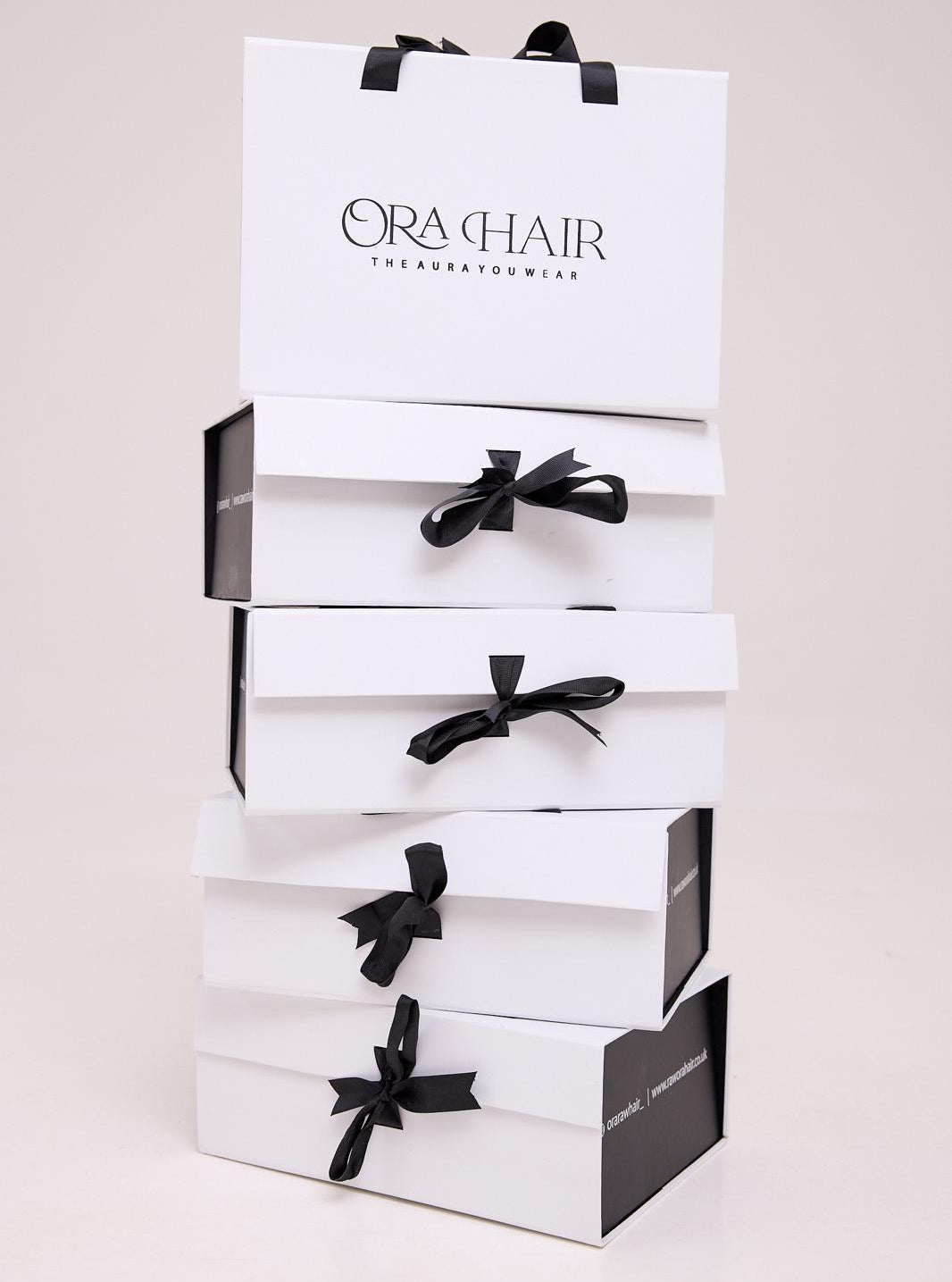 Stack of white boxes with black bows and 'Ora Hair' branding on a light background